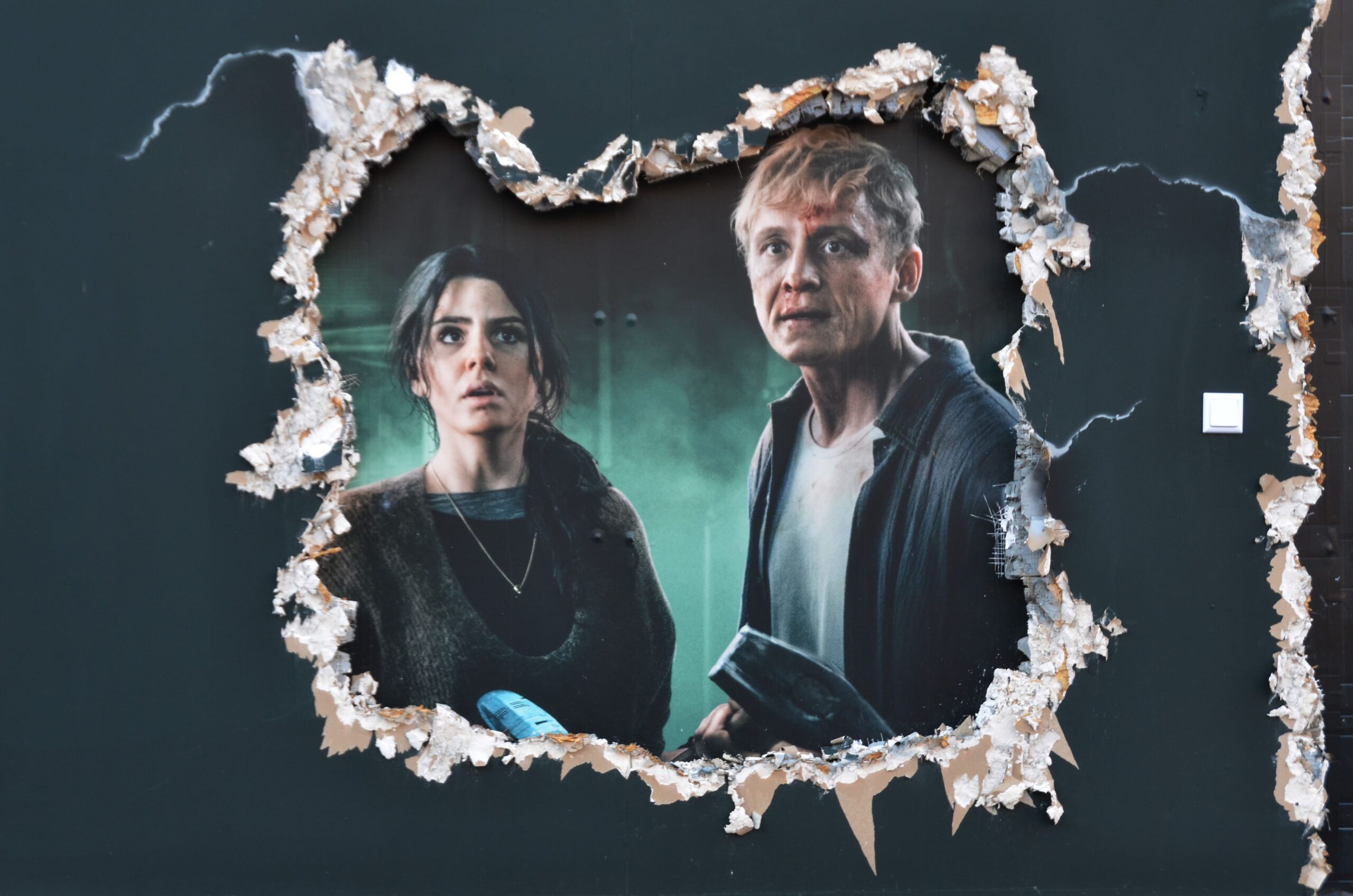 Detailaufnahme der Bauzaunkunst von CONCRETE CANDY für Netflix „Brick“, mit realistisch gemalten Risskanten und Filmszene durch die Wand hindurch sichtbar.