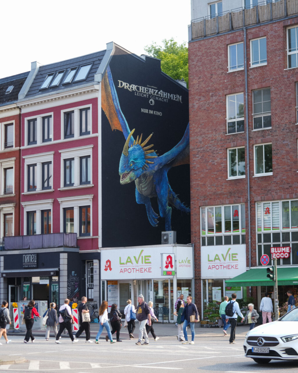 Fassadenmalerei eines blauen Drachen zwischen zwei Stadthäusern als aufmerksamkeitsstarke Kinokampagne im urbanen Raum.