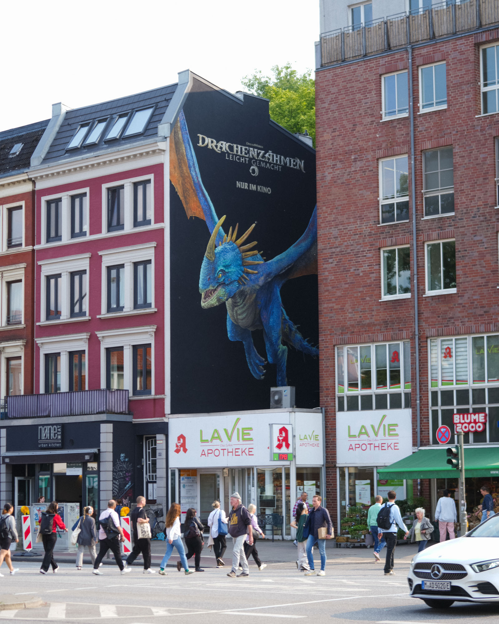 Fassadenmalerei eines blauen Drachen zwischen zwei Stadthäusern als aufmerksamkeitsstarke Kinokampagne im urbanen Raum.