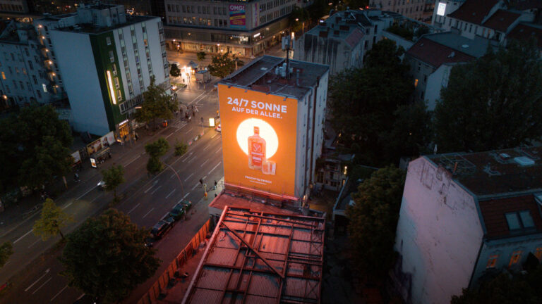 Luftaufnahme der Berliner Sonnenallee bei Nacht mit großem, beleuchtetem Jägermeister-3D-Mural auf einer Hauswand.