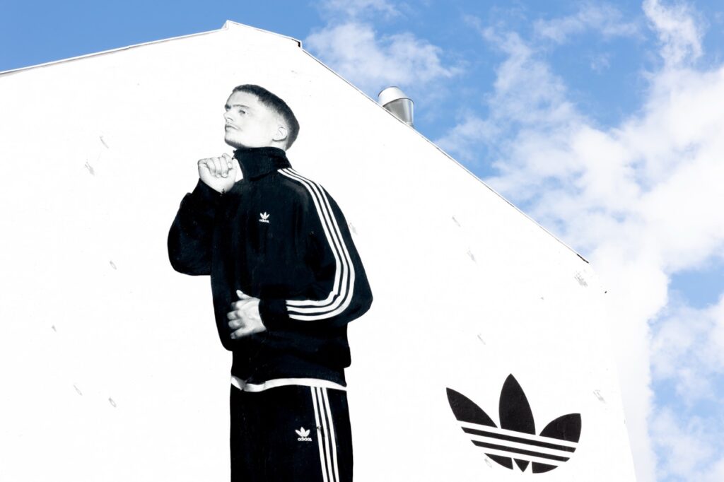 Detailaufnahme eines fotorealistischen Adidas-Murals mit Florian Wirtz im schwarzen Tracksuit vor weißem Hintergrund.