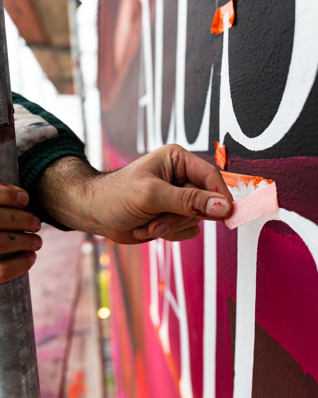 Detailaufnahme einer Hand beim Abkleben von Typografie auf einer bemalten Wand für ein großflächiges Mural