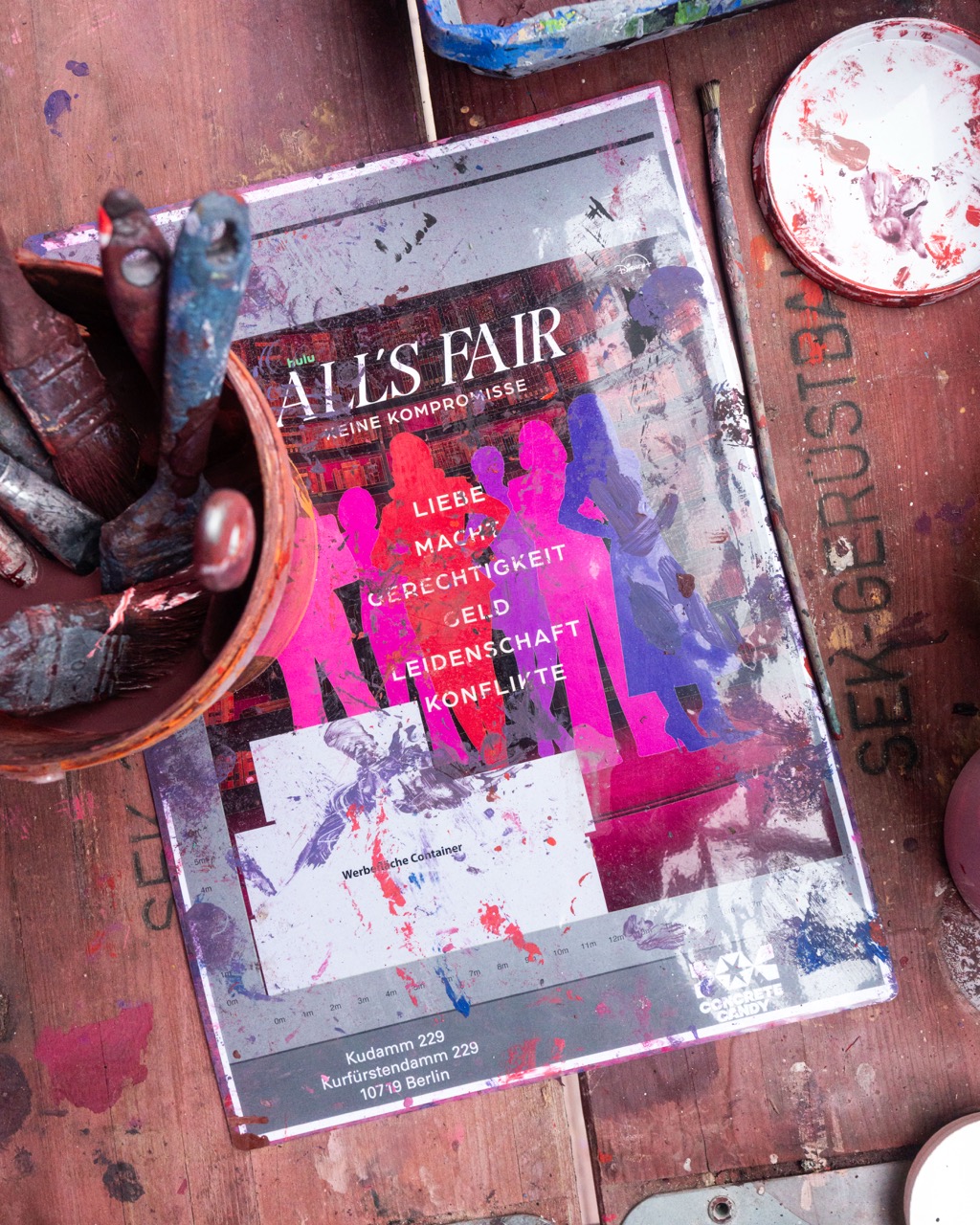 Ausgedrucktes Mural-Layout für die Disney+ Kampagne All’s Fair neben Pinseln und Farbe auf einer Arbeitsfläche