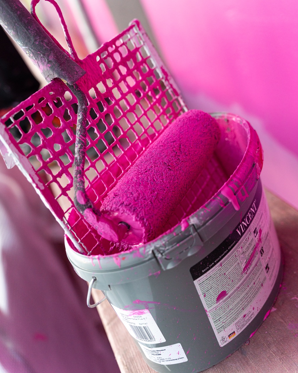 Farbrolle mit leuchtend pinker Farbe in einem Eimer während der Umsetzung eines Murals