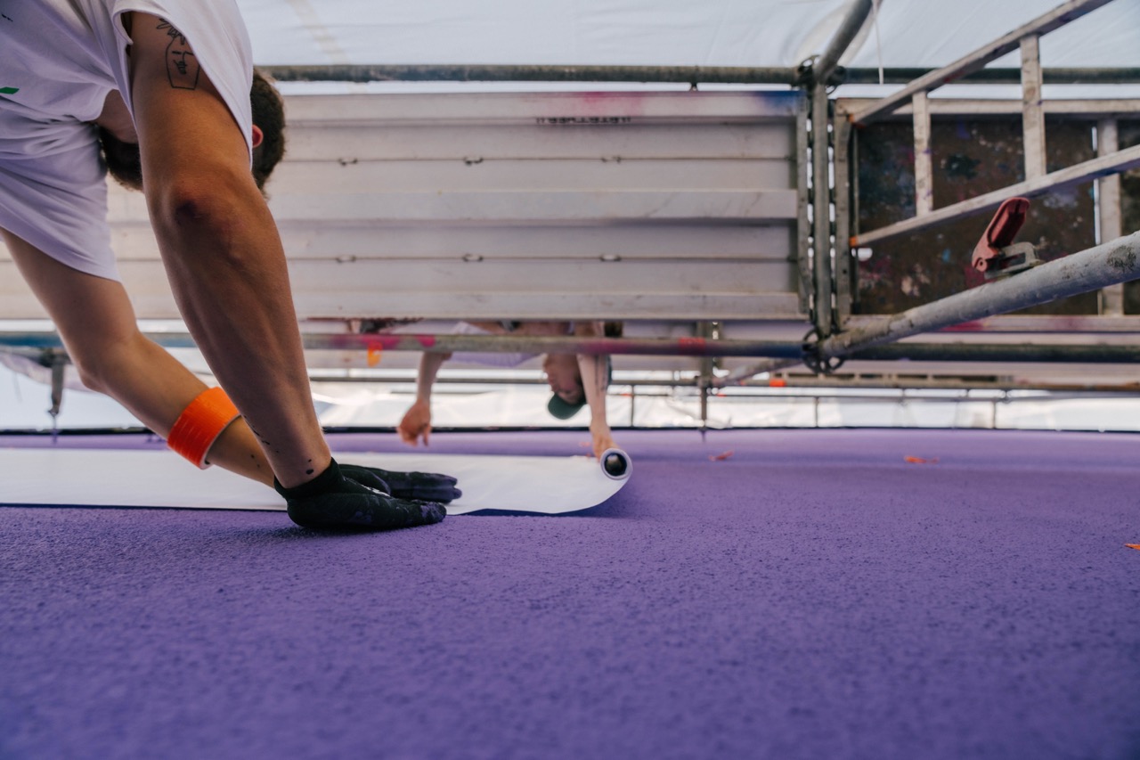 Künstler bringt großflächige Folie auf violett gestrichter Wand unter einem Gerüst an