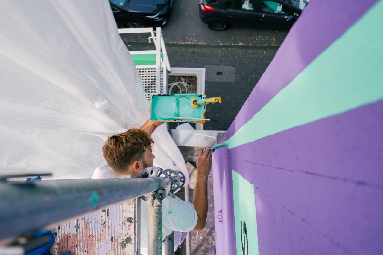Künstler malt farbige Linien auf violette Wand aus erhöhter Perspektive
