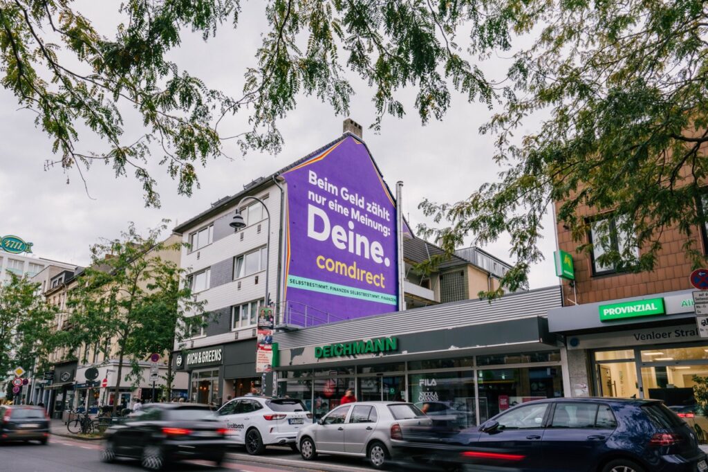 Großflächiges Comdirect Mural an einer Hausfassade in Köln-Ehrenfeld an der Venloer Straße mit vorbeifahrendem Verkehr