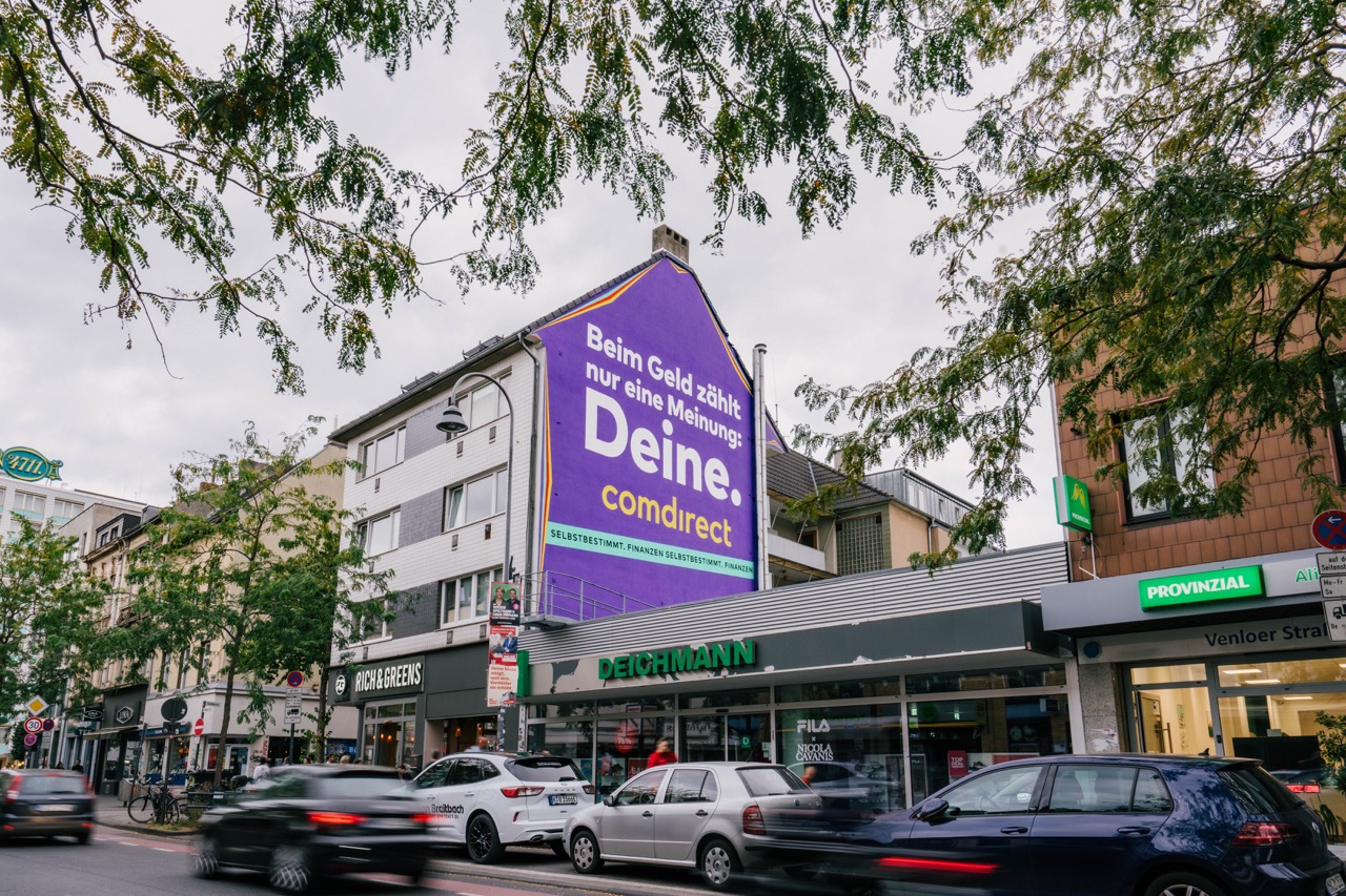 Großflächiges Comdirect Mural an einer Hausfassade in Köln-Ehrenfeld an der Venloer Straße mit vorbeifahrendem Verkehr