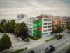 Weitwinkelaufnahme des fertigen S-Bahn München Murals an der Gebäudefassade mit vorbeifahrenden Autos und dichter Wohnbebauung.