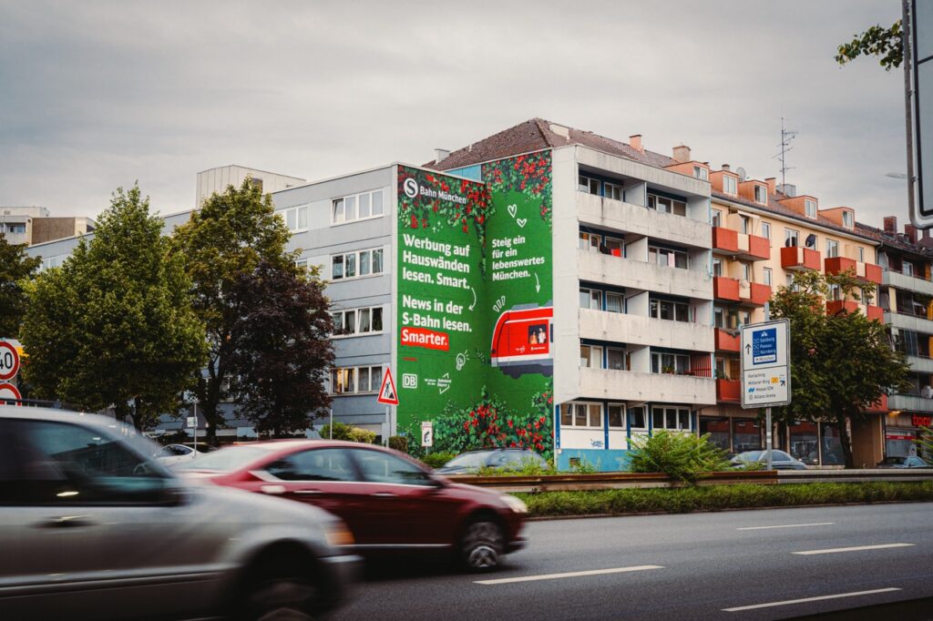 Frontale Aufnahme des S-Bahn München Murals mit vorbeifahrenden Autos auf der Tegernseer Landstraße in München.