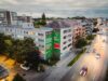 Drohnenaufnahme des beleuchteten S-Bahn München Murals in der Abenddämmerung mit Lichtspuren des Verkehrs auf der Tegernseer Landstraße.