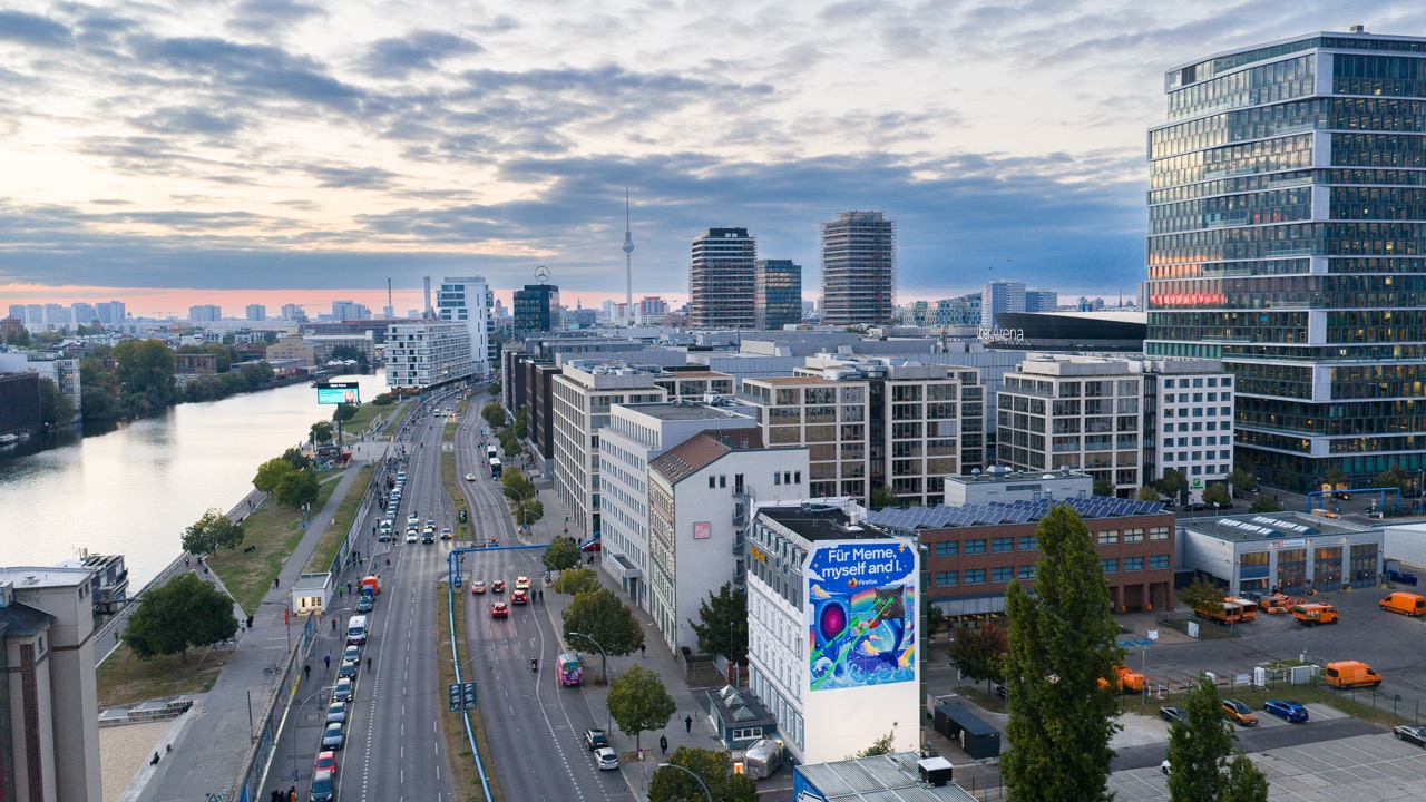 Luftaufnahme eines großflächigen Firefox Murals an einer Gebäudefassade entlang der Spree in Berlin mit Blick auf Stadtlandschaft und Fernsehturm.