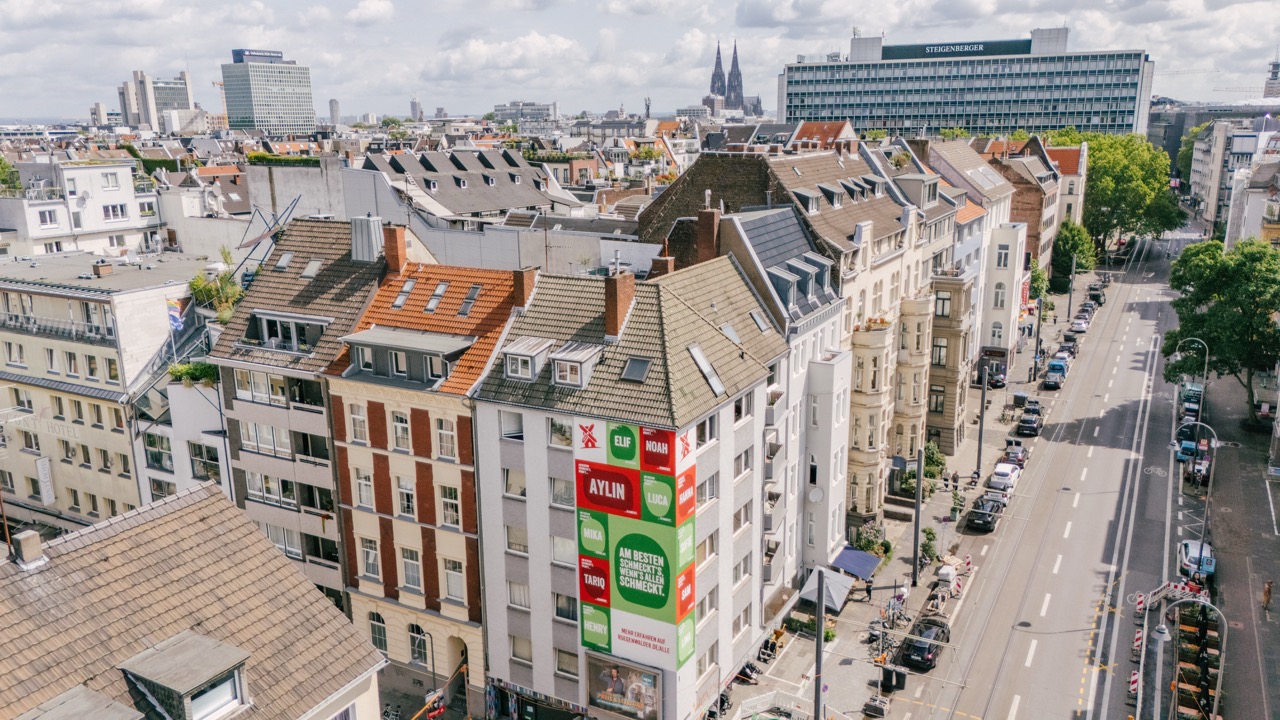Luftaufnahme eines Murals im Belgischen Viertel in Köln mit Blick über Dächer und Kölner Dom im Hintergrund.