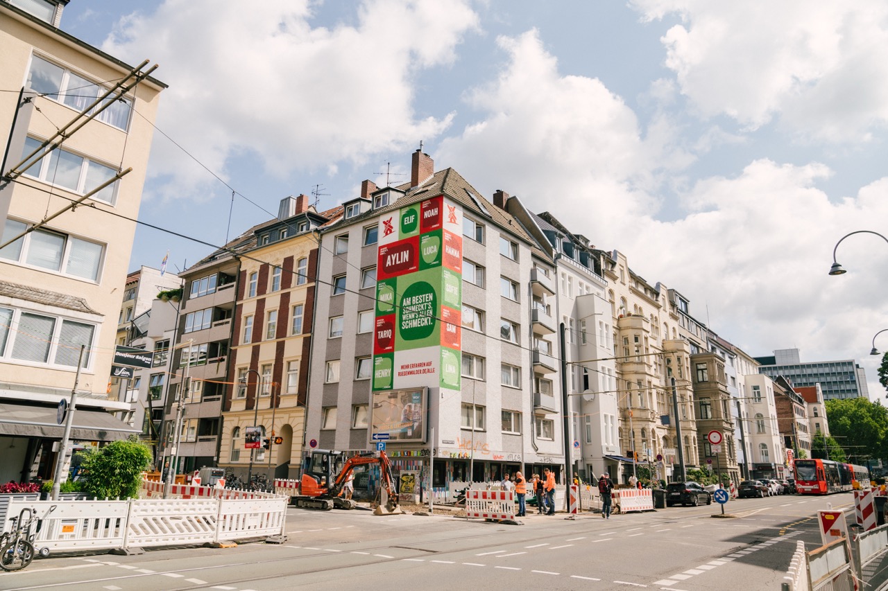 Großflächiges Mural an einer Hausfassade im Belgischen Viertel in Köln mit farbigen Flächen und Namen.