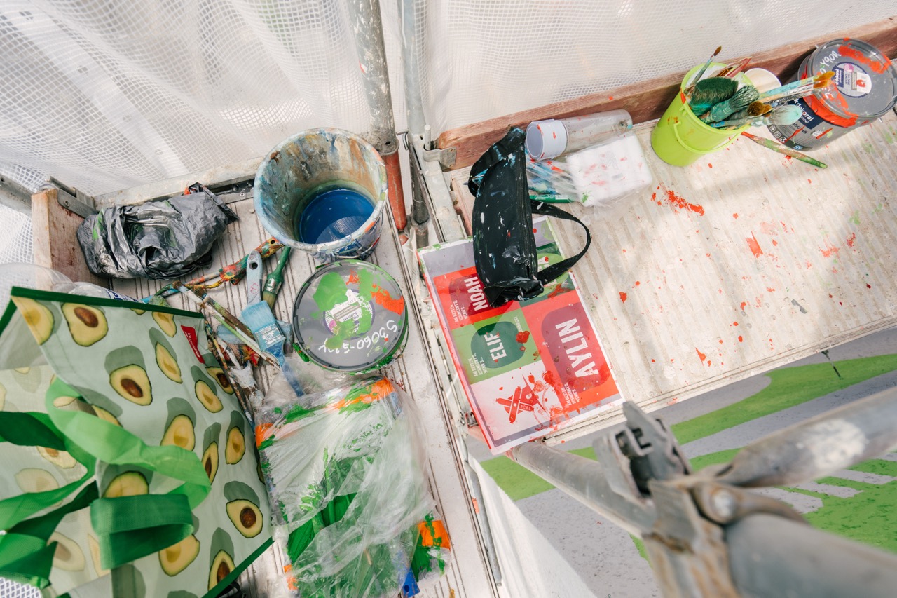 Malerutensilien wie Farbeimer, Pinsel und Werkzeuge liegen auf einem Gerüstboden.