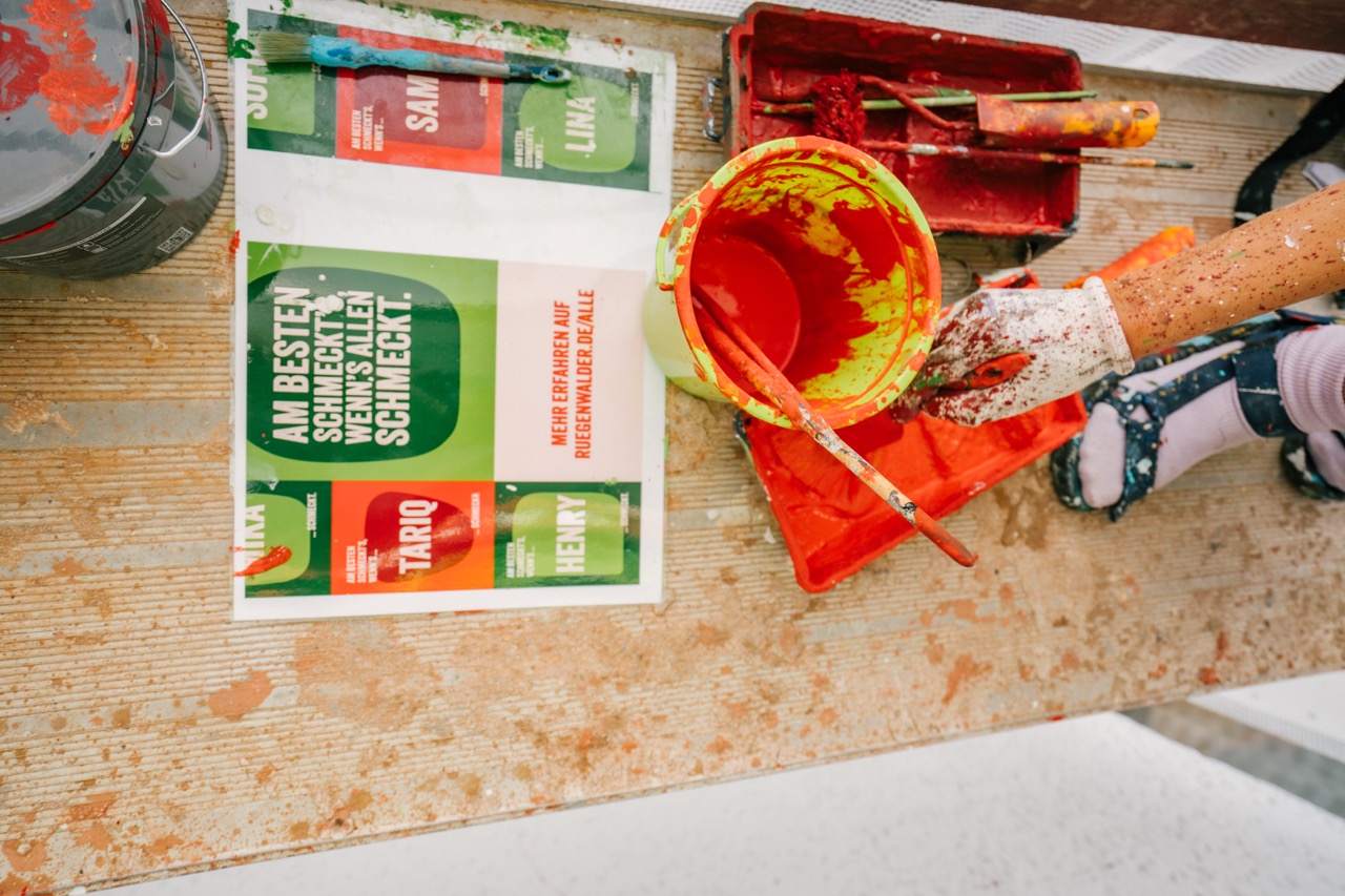 Detailaufnahme von Farbeimern und Pinseln mit leuchtend roter Farbe auf einem Gerüst.