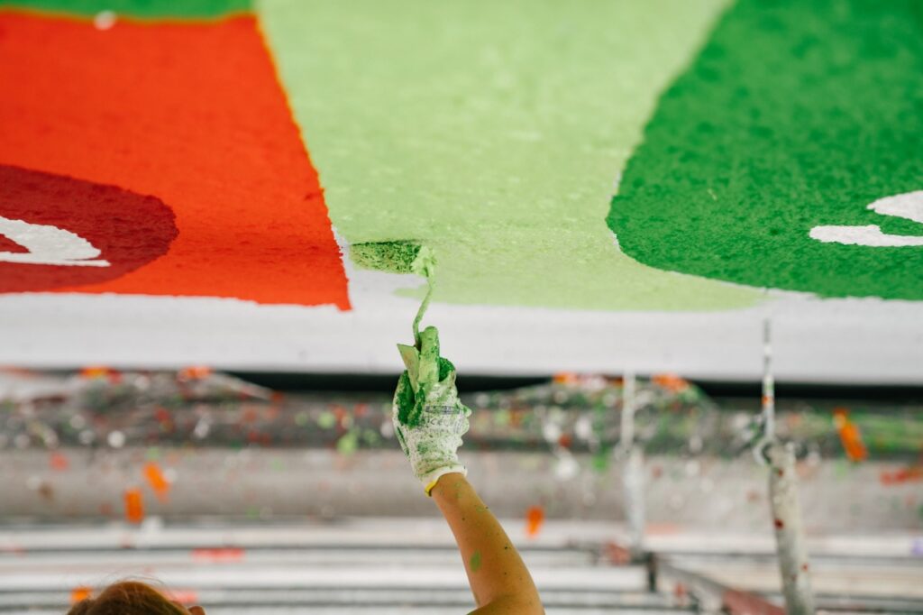 Hand mit Farbroller trägt grüne Farbe präzise auf eine Wandfläche auf.
