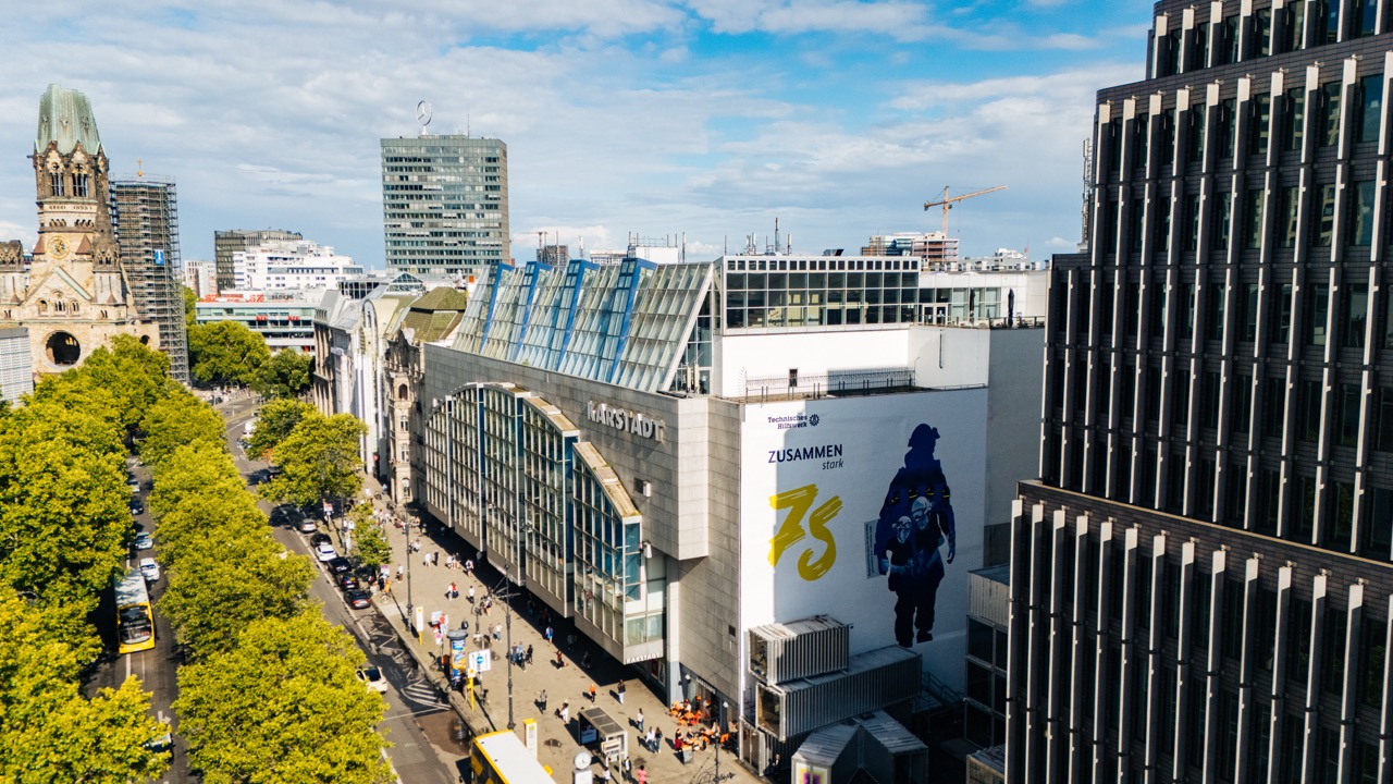 Luftaufnahme des Kurfürstendamms in Berlin mit großflächigem THW-Mural an einer Gebäudefassade.