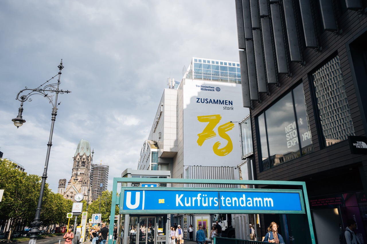Straßenszene am Kurfürstendamm mit U-Bahn-Schild und großem THW-Mural an einer Gebäudewand.