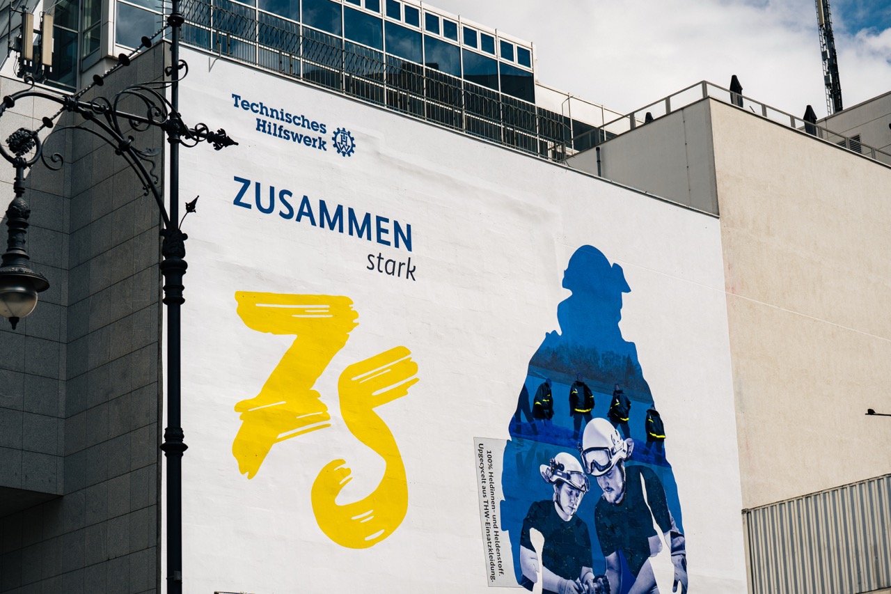 Großes THW-Mural mit Schriftzug „Zusammen stark“ und gelber 75 auf weißer Fassade in Berlin.