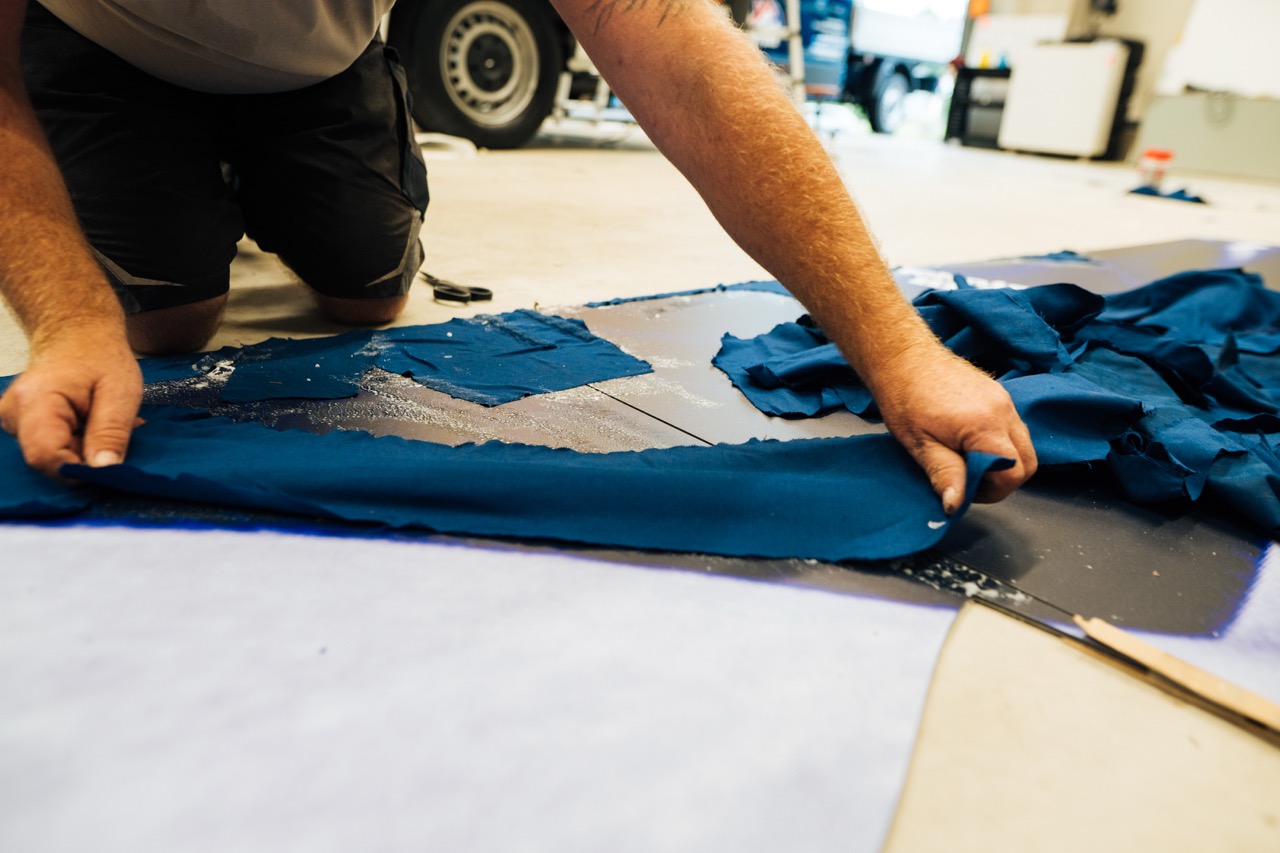 Hände schneiden und bearbeiten blauen Stoff auf einem Arbeitstisch als Vorbereitung für das Mural.