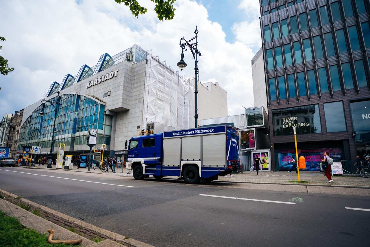 Straßenszene am Kurfürstendamm in Berlin mit THW-Fahrzeug vor einer eingerüsteten Fassade.