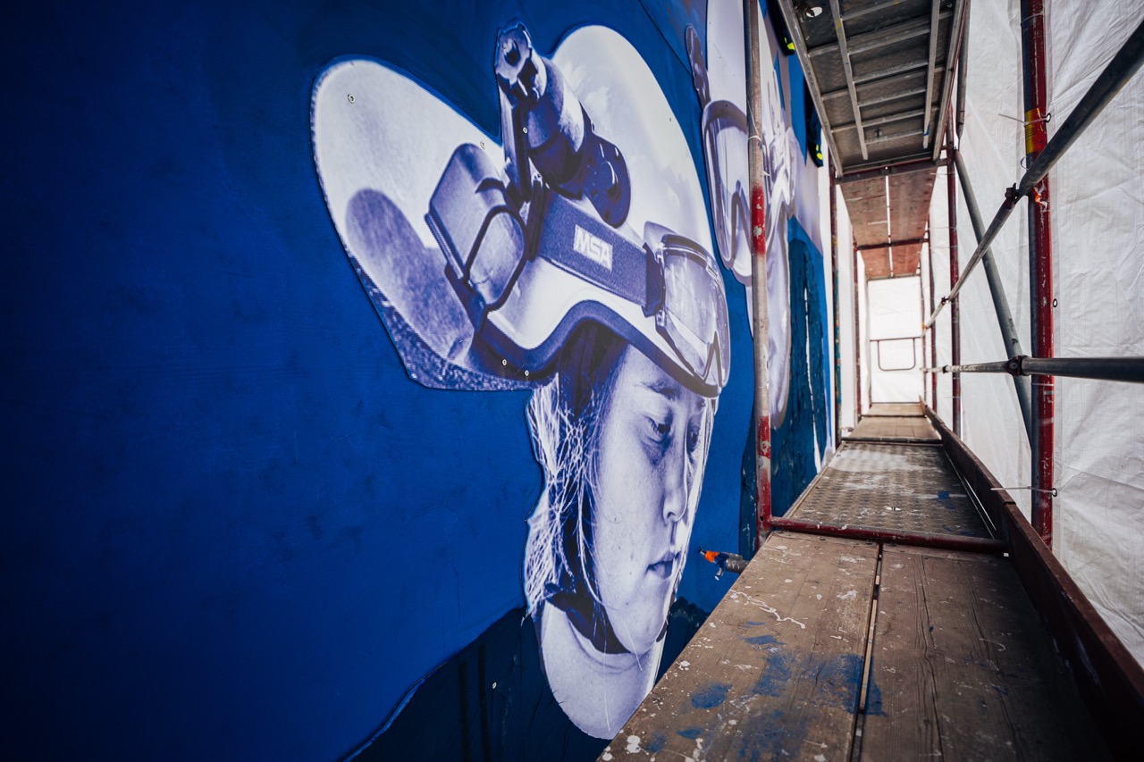 Teil eines großflächigen Murals mit porträtierter Person und THW-Helm, aufgenommen vom Gerüst aus.