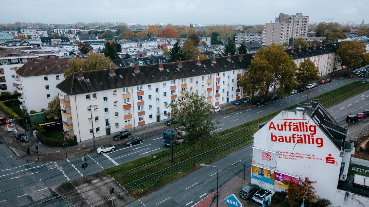 Luftaufnahme eines Wohngebiets mit Sparkassen-Mural auf einer Giebelwand an einer Straße mit Straßenbahn.