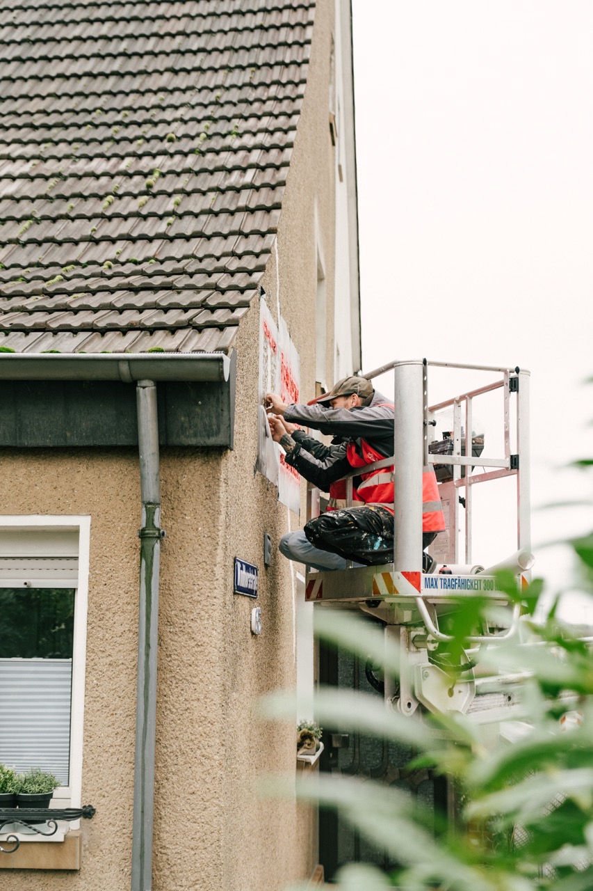 Person befestigt einen QR-Code an einer Hauswand von einer Hebebühne aus.