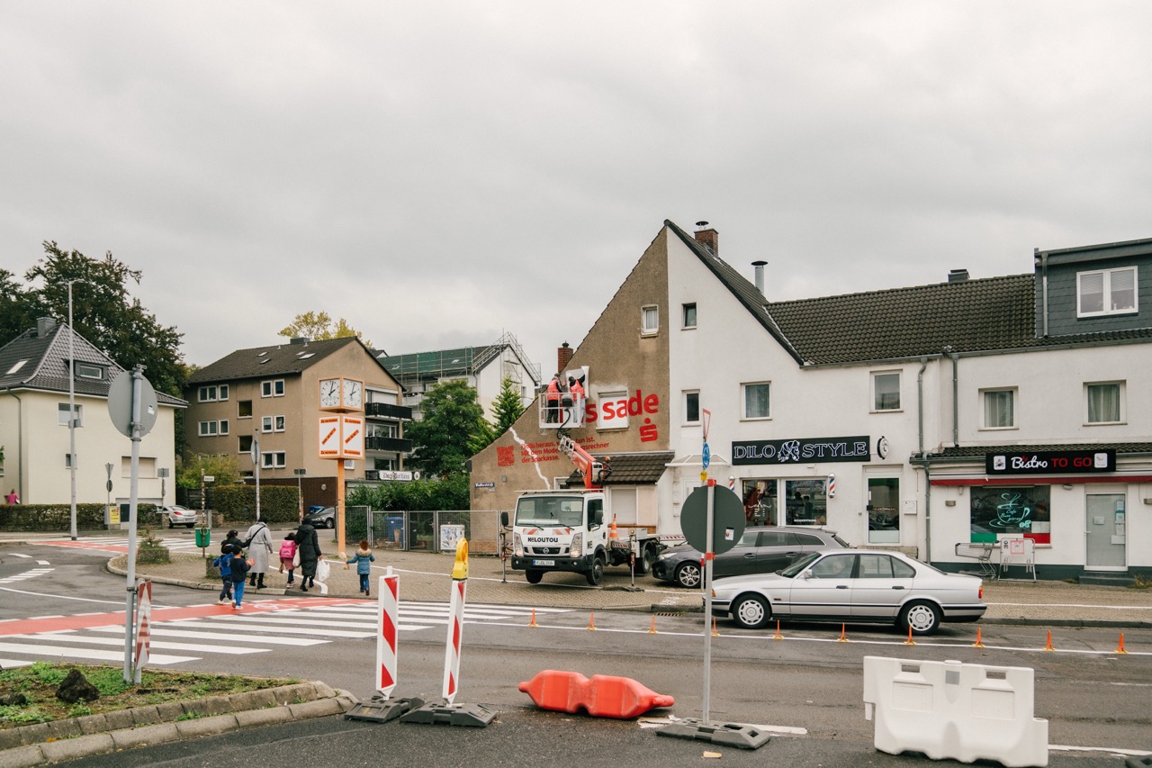 Straßenszene mit Hebebühne und entstehendem Sparkassen-Mural an einer Hauswand.
