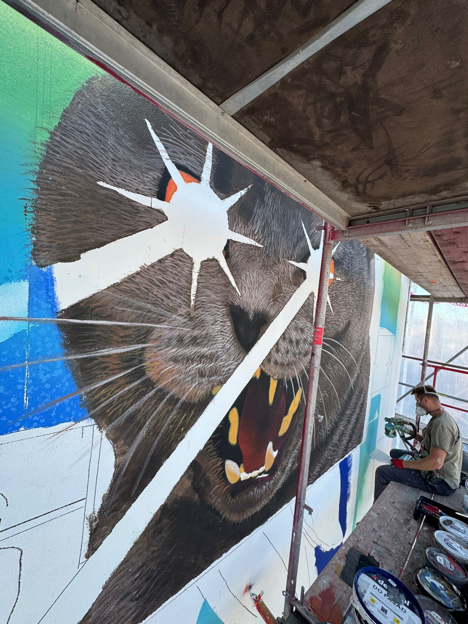 Großflächiges Mural zeigt einen detailliert gemalten Fuchs mit aufgerissenem Maul, umgeben von geometrischen Formen und dynamischen Elementen, während der Künstler auf dem Gerüst arbeitet.