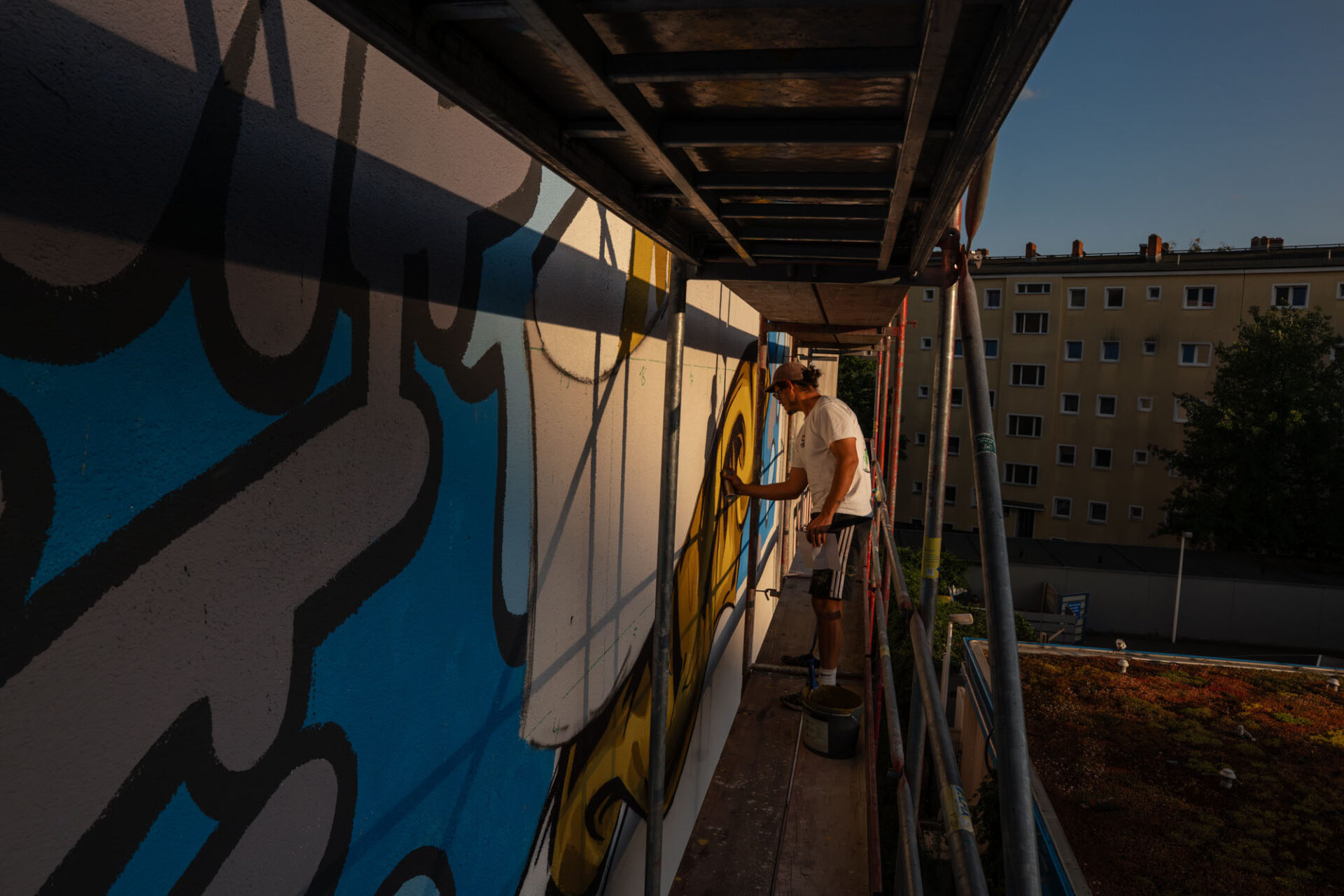Künstler malt ein großes Hertha-BSC-Mural an einer Hausfassade in Berlin von einem Gerüst aus.