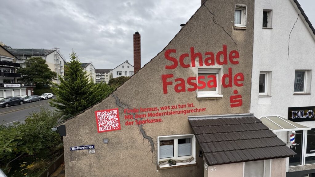 Detail einer Hauswand mit Sparkassen-QR-Code und Text zum Modernisierungsrechner.