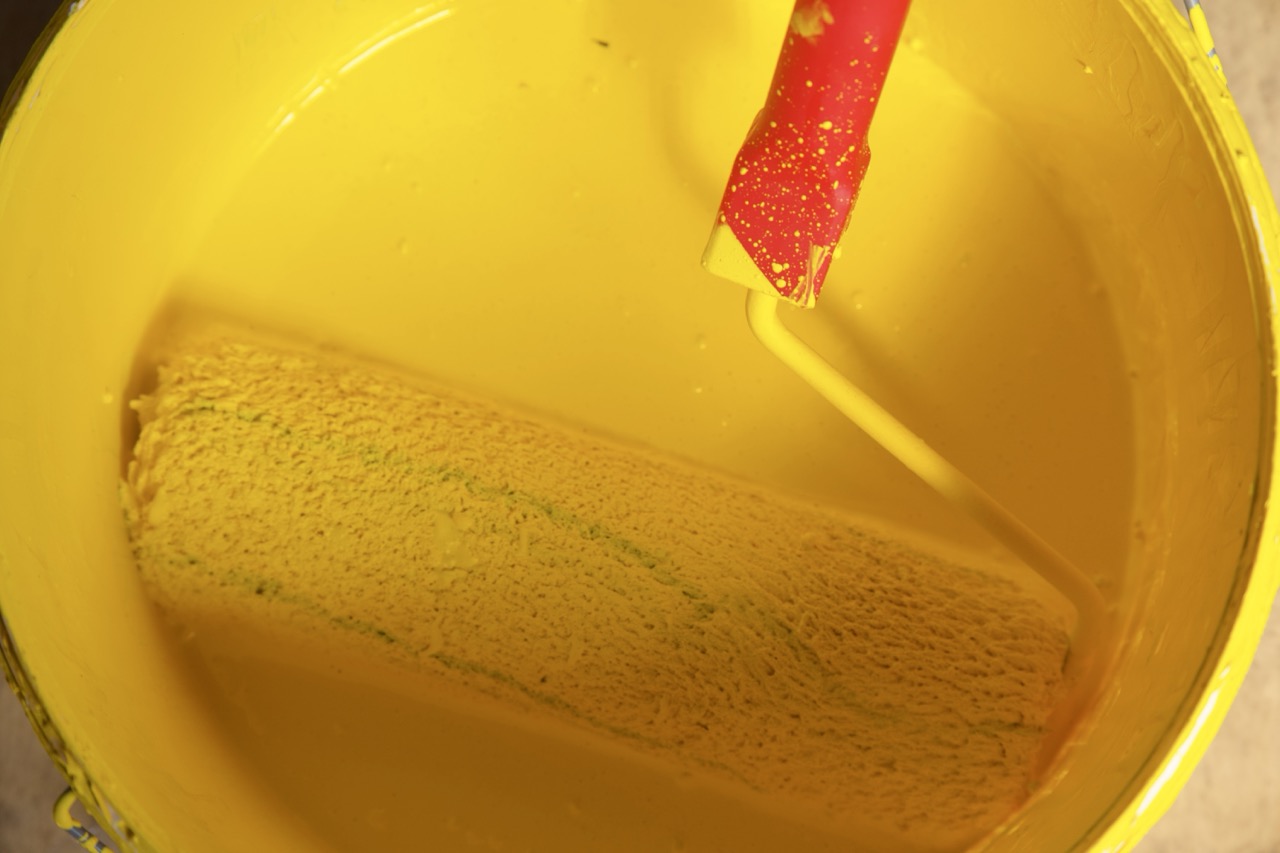 Farbrolle liegt in einem Eimer mit leuchtend gelber Farbe, bereit für die Beschichtung der 3D-Objekte.