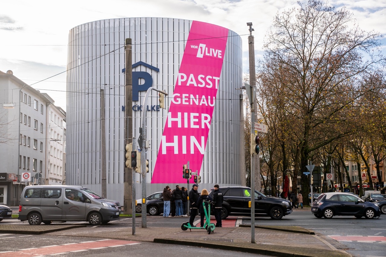 Großflächige 1LIVE Werbung mit pinkem Banner und weißer Typografie an der Fassade eines Parkhauses in Dortmund an einer belebten Straßenkreuzung