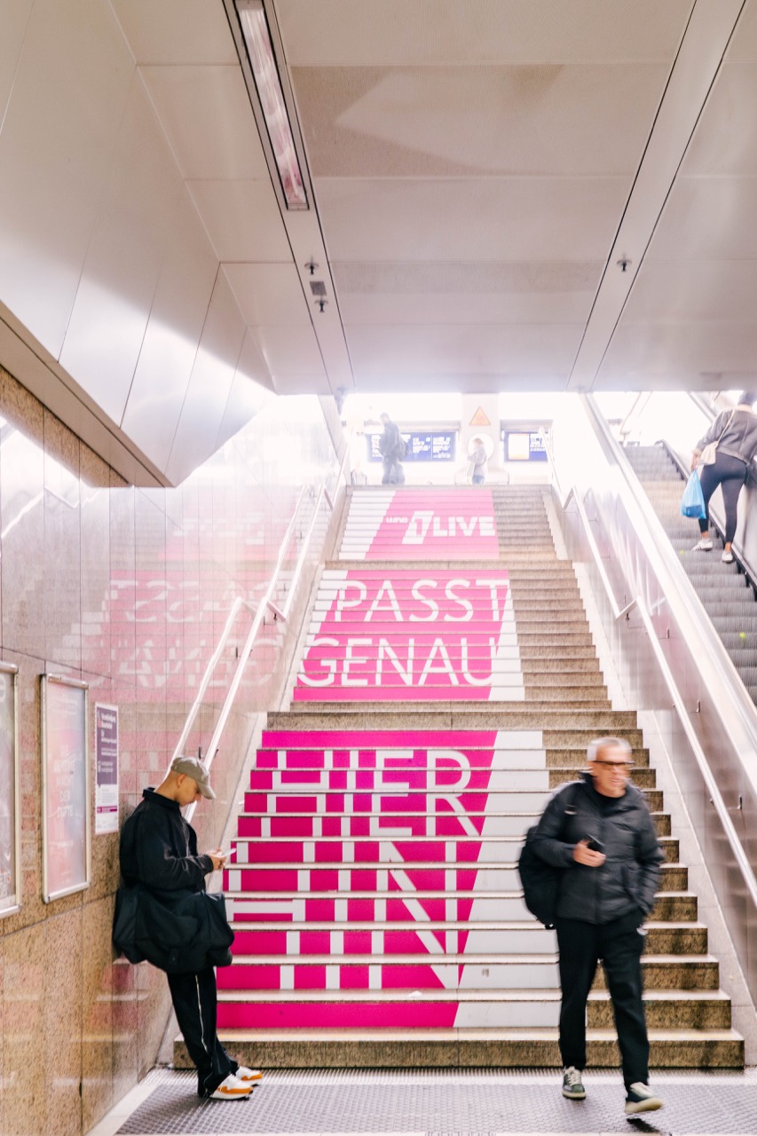 1LIVE Treppenbeklebung in Düsseldorf mit zentraler Perspektive und vorbeigehenden Menschen im Bewegungsunschärfe