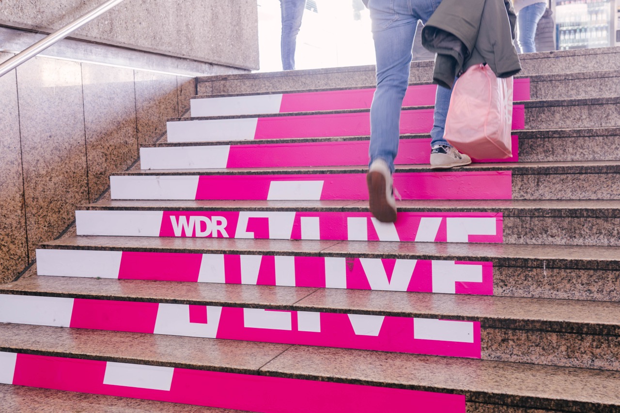Detailaufnahme einer Treppenbeklebung mit 1LIVE Schriftzug auf pink-weißen Stufen in Düsseldorf