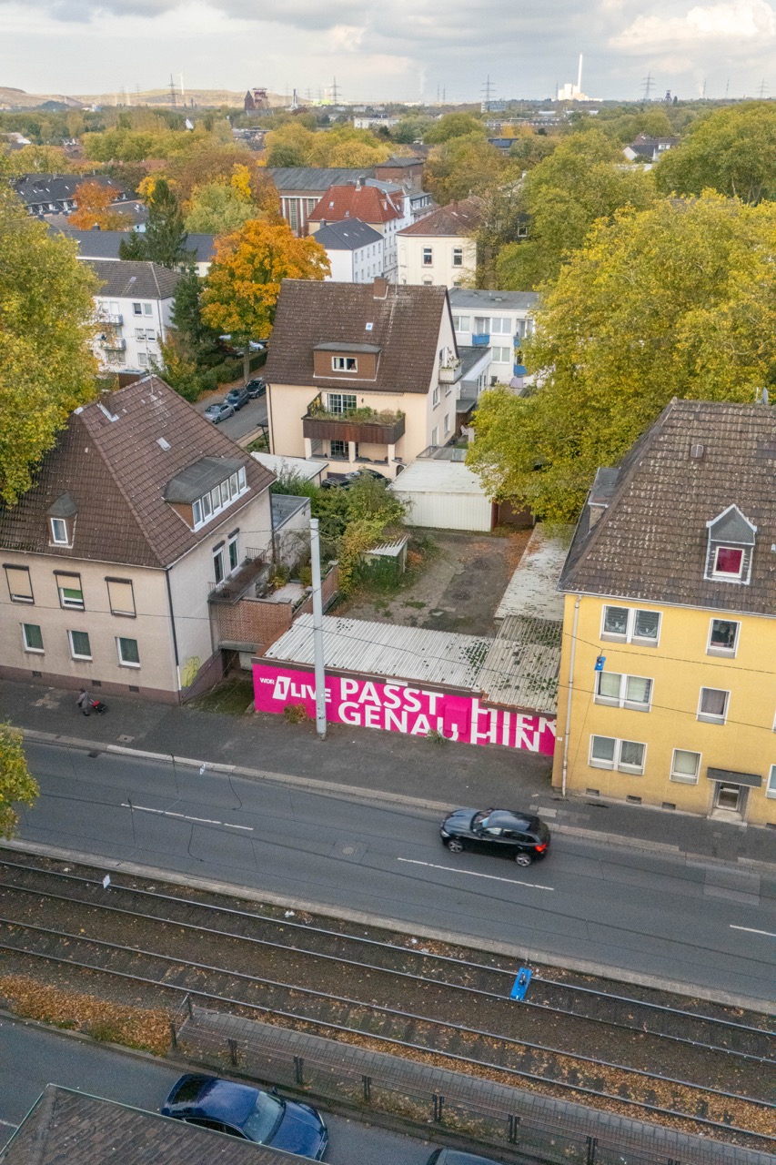 Luftaufnahme eines pinken 1LIVE Murals entlang einer Straße in Gelsenkirchen mit Wohnhäusern und Bahntrasse im Vordergrund