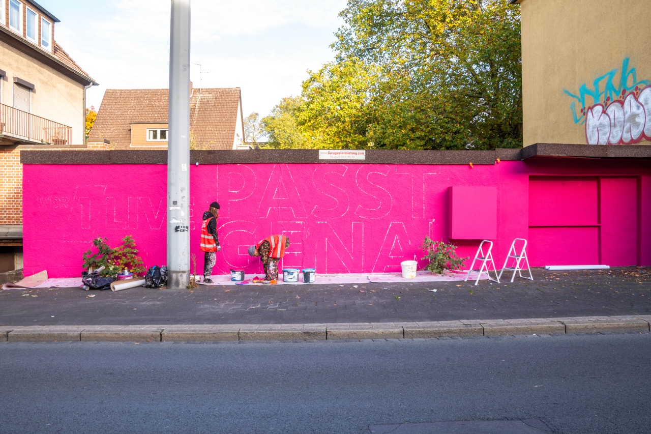 Künstlerinnen und Künstler skizzieren ein großes 1LIVE Mural auf pink grundierter Wand in Gelsenkirchen
