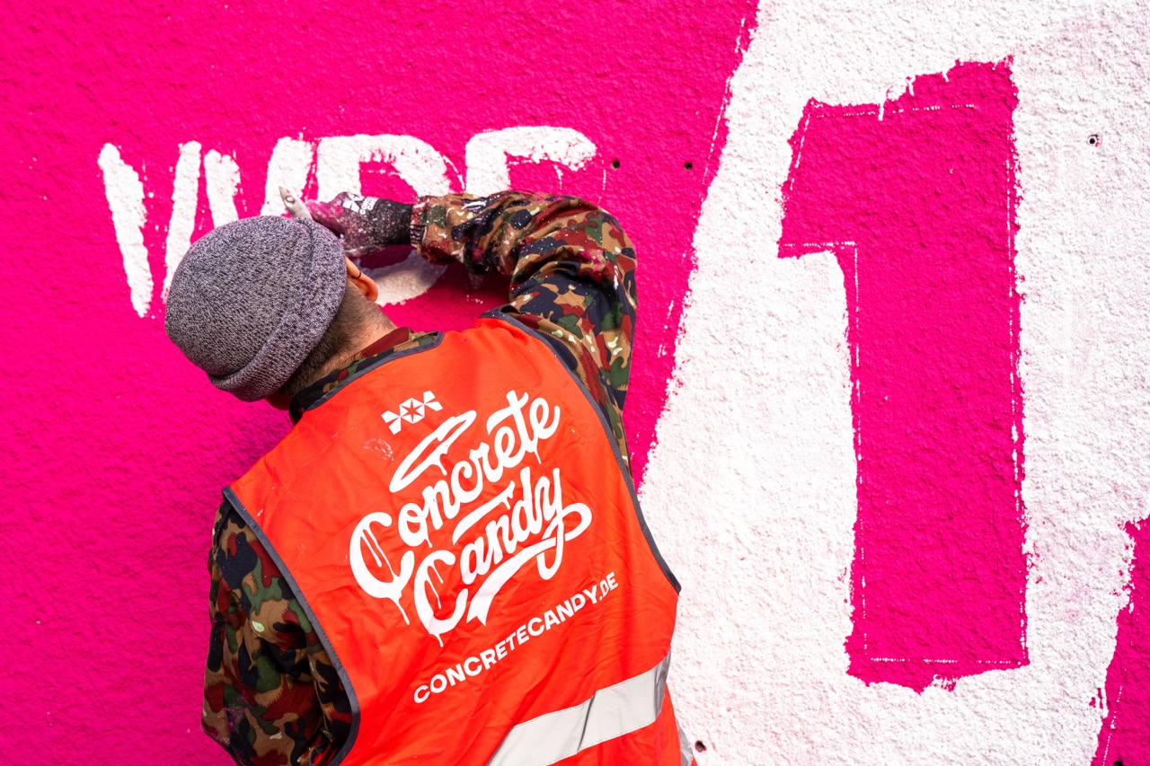 Künstler malt weiße Typografie auf pinkem Hintergrund eines 1LIVE Murals in Nahaufnahme