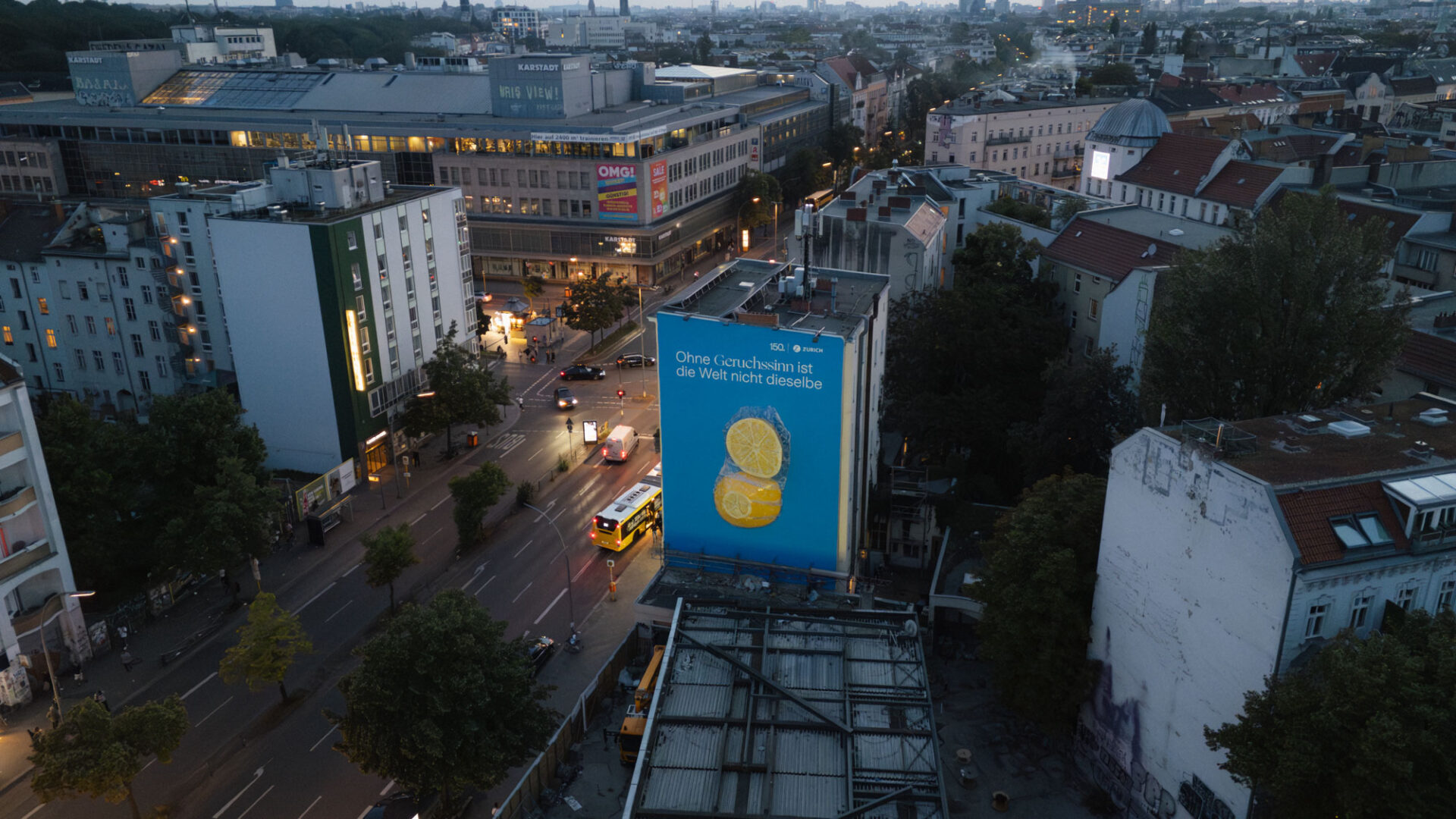 Luftaufnahme der Sonnenallee in Berlin bei Dämmerung mit großflächigem Mural auf einer Hausfassade, das zwei Zitronen vor blauem Hintergrund zeigt.