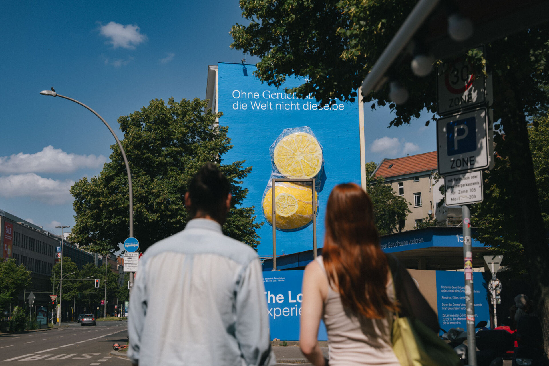 Zwei Personen betrachten ein großflächiges Mural mit Zitronen an einer Hausfassade in Berlin bei Tageslicht.