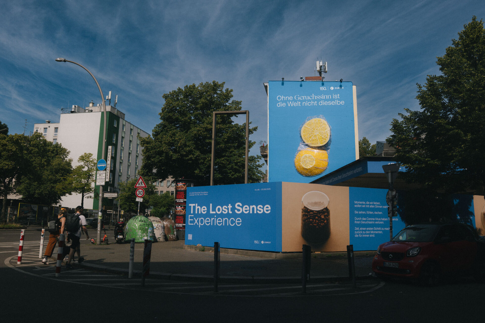 Straßenszene bei Tageslicht mit großem Mural und begleitender Installation „The Lost Sense Experience“ vor einem Gebäude in Berlin.