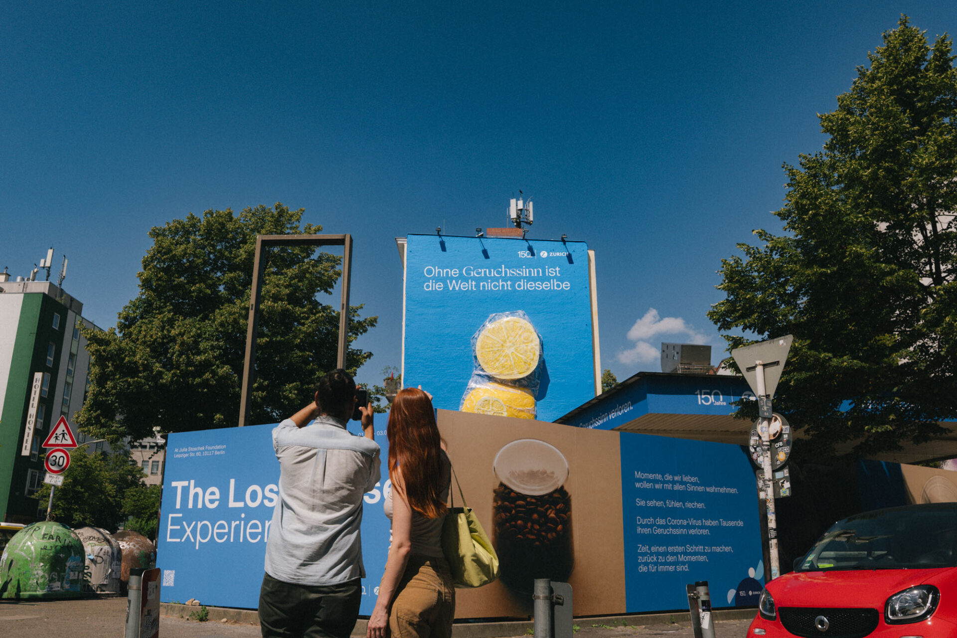 Zwei Personen fotografieren ein großes Zitronen-Mural an einer Gebäudefassade, das Teil einer urbanen Installation ist.