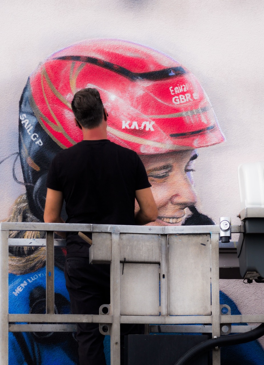 Künstler TANK malt ein realistisches Porträt eines SailGP-Athleten mit rotem Helm als Teil des Murals.