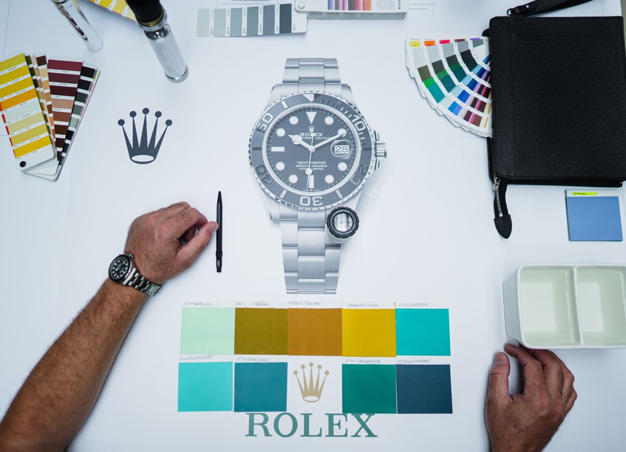 Arbeitssetup mit Entwurf einer Rolex Yacht-Master Uhr, umgeben von Farbmustern, Tools und Referenzen zur Planung des Murals.