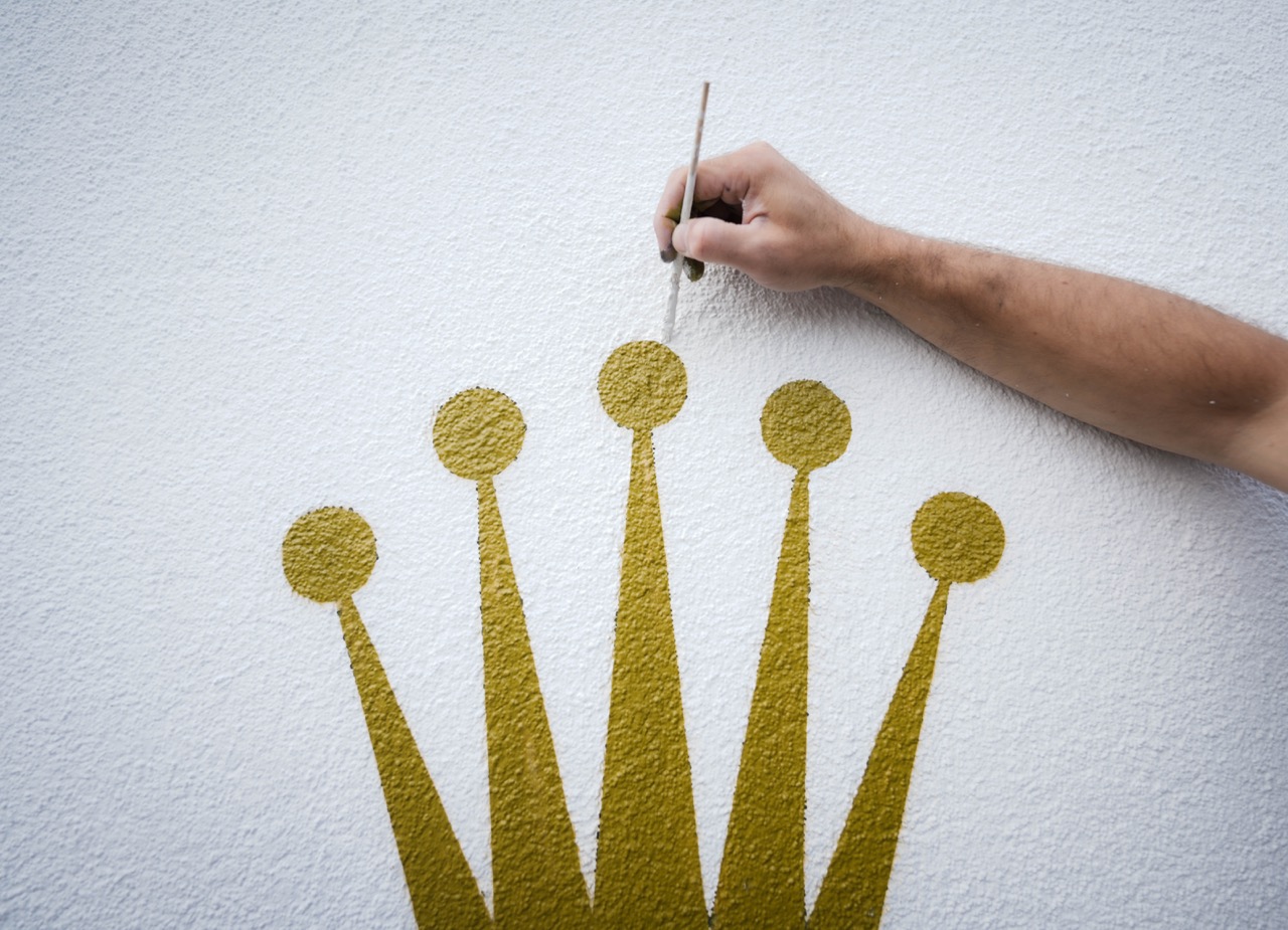 Detailaufnahme, wie die Rolex Krone sorgfältig mit Pinsel auf die Wand gemalt wird.