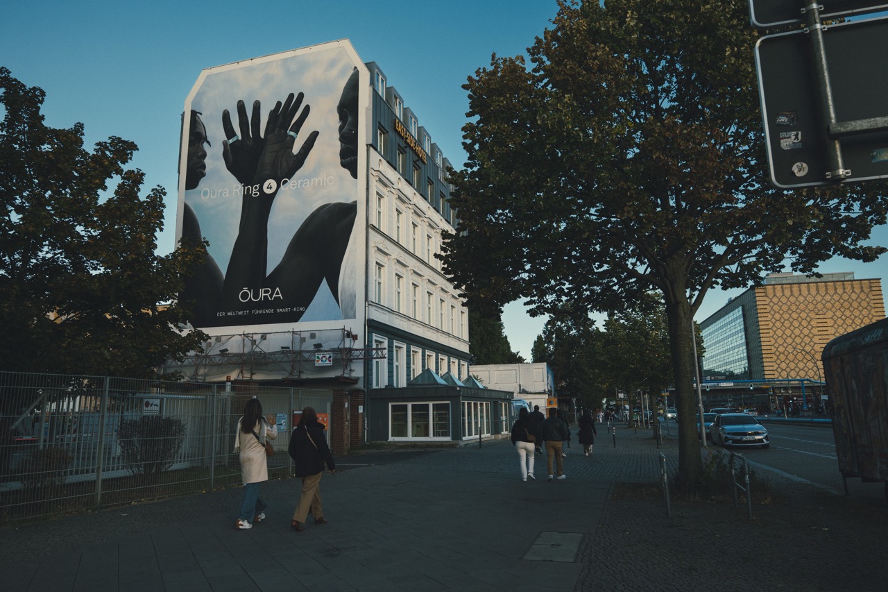 Straßenansicht des East Side Hotels mit Oura Mural und Passanten auf dem Gehweg.