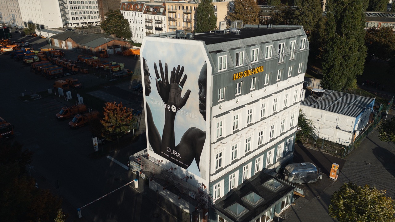 Drohnenaufnahme des East Side Hotels in Berlin mit großflächigem Oura Ring 4 Ceramic Mural an der Gebäudeseite.