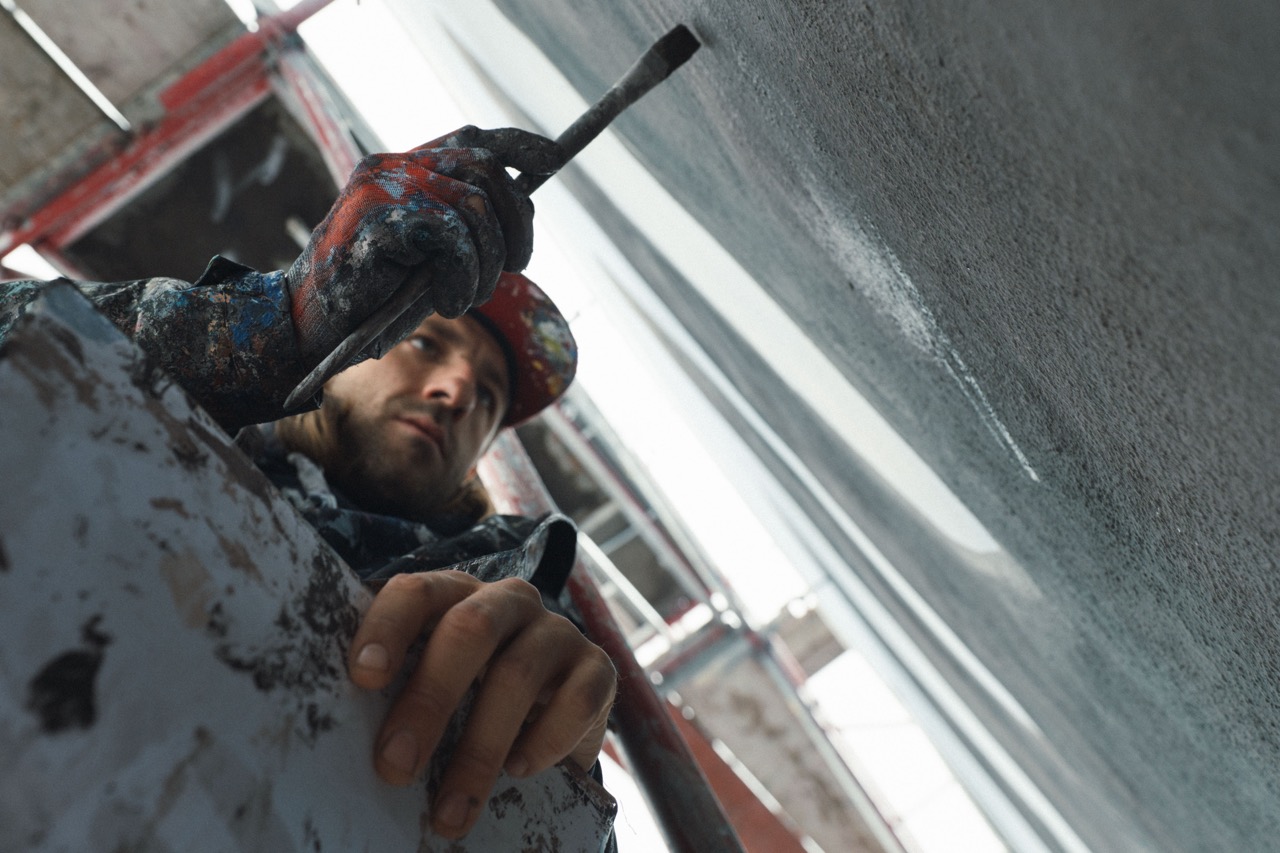 Detailaufnahme eines Künstlers beim präzisen Auftragen von Farbe mit Pinsel auf die Wand eines Murals.